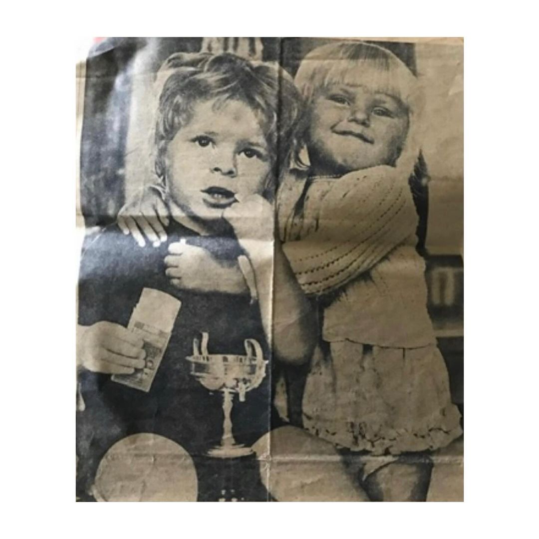 Retro newspaper photo of two smiling children, one holding what looks like an award, in grainy black and white with visible paper texture.