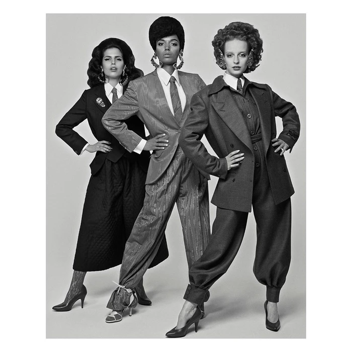 Three female models posing in tailored suits and voluminous retro hairstyles against a plain studio background.