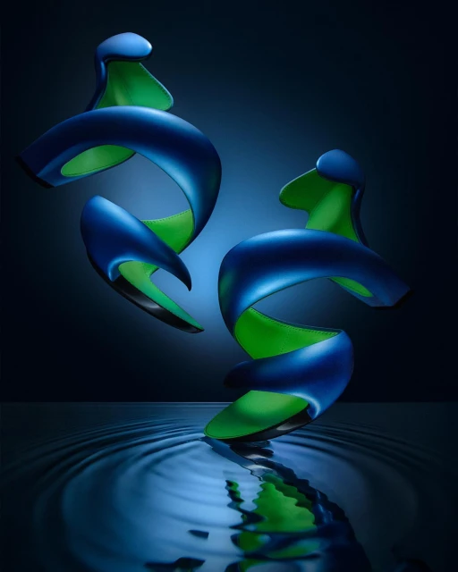Abstract art still life featuring two swirling, intertwined blue and green objects reflected in rippling water against a dark backdrop.