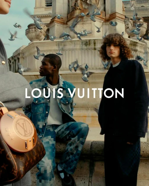 Louis Vuitton fashion advertisement featuring two male models in patterned clothing with a purse, pigeons, and a building backdrop.