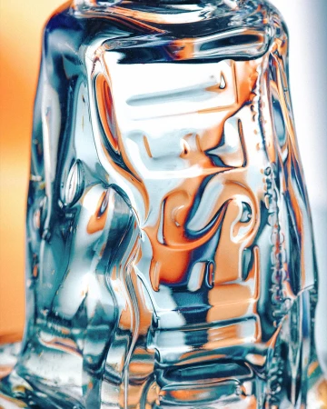 Close-up of a textured clear glass with abstract shapes, showcasing patterns of light and refraction against an orange and white background.
