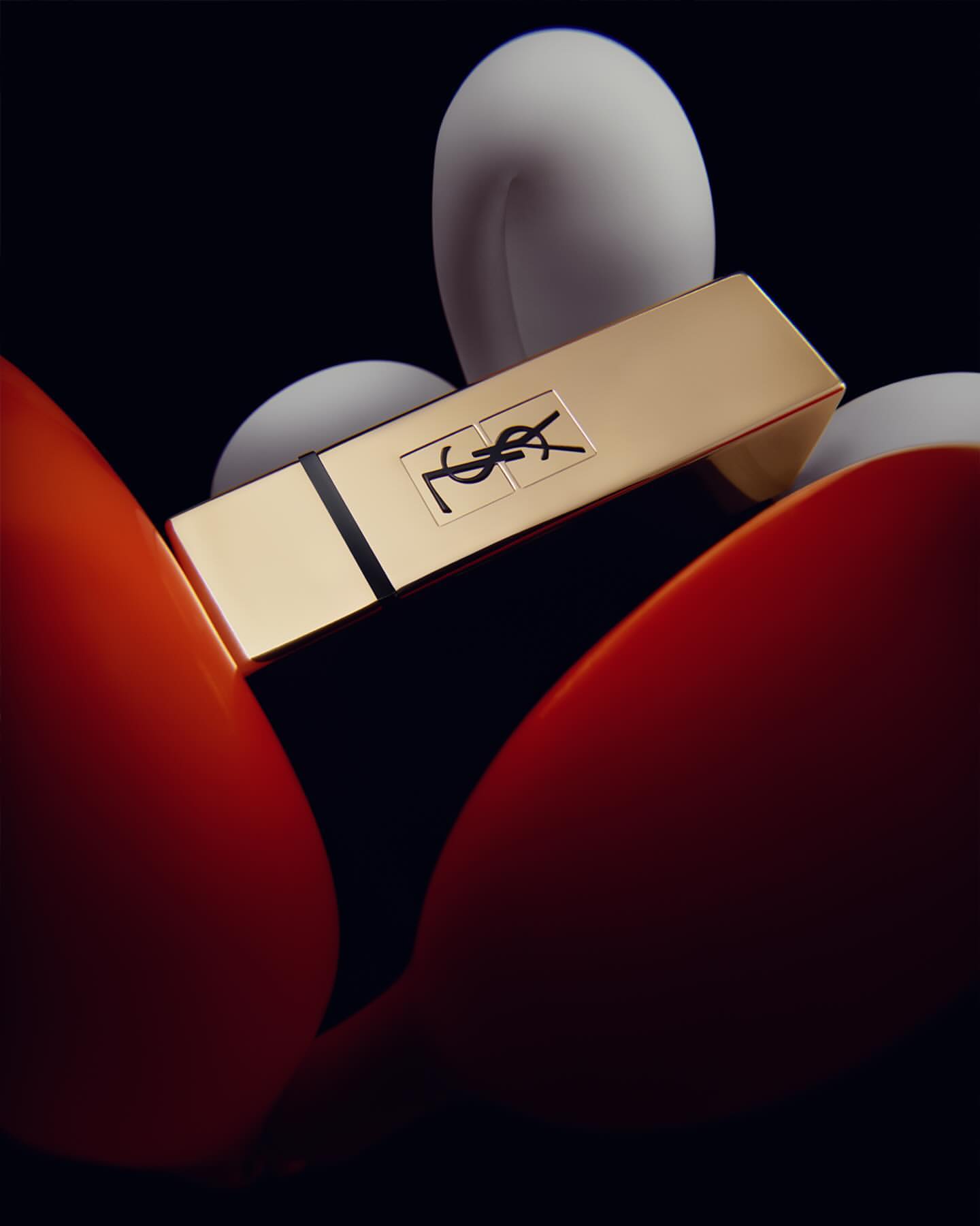Close-up studio shot of a gold Yves Saint Laurent lipstick with orange and white accents against a dark backdrop. Beauty, fashion, product.
