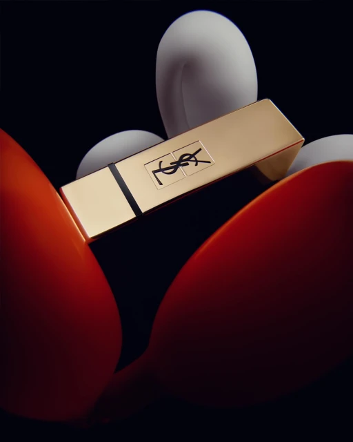 Close-up studio shot of a gold Yves Saint Laurent lipstick with orange and white accents against a dark backdrop. Beauty, fashion, product.