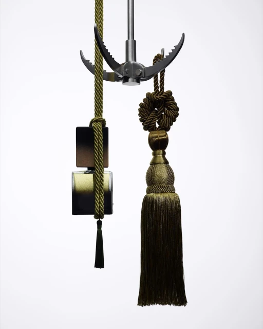 Conceptual display of a dark-toned perfume bottle suspended by decorative ropes and a metallic grappling hook against a bright white background.