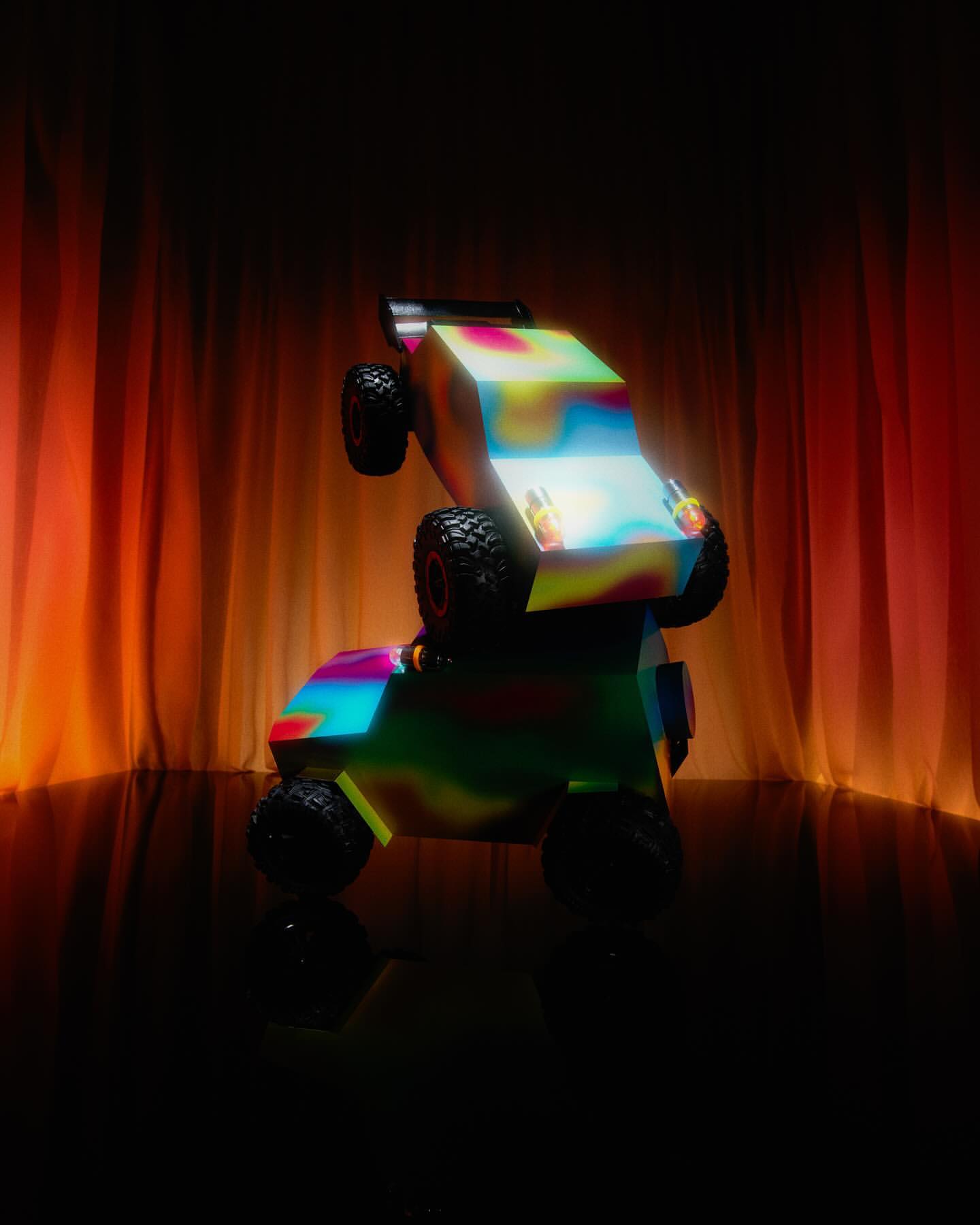 Two toy cars stacked on top of each other against a softly lit orange curtain backdrop create an abstract automotive scene.