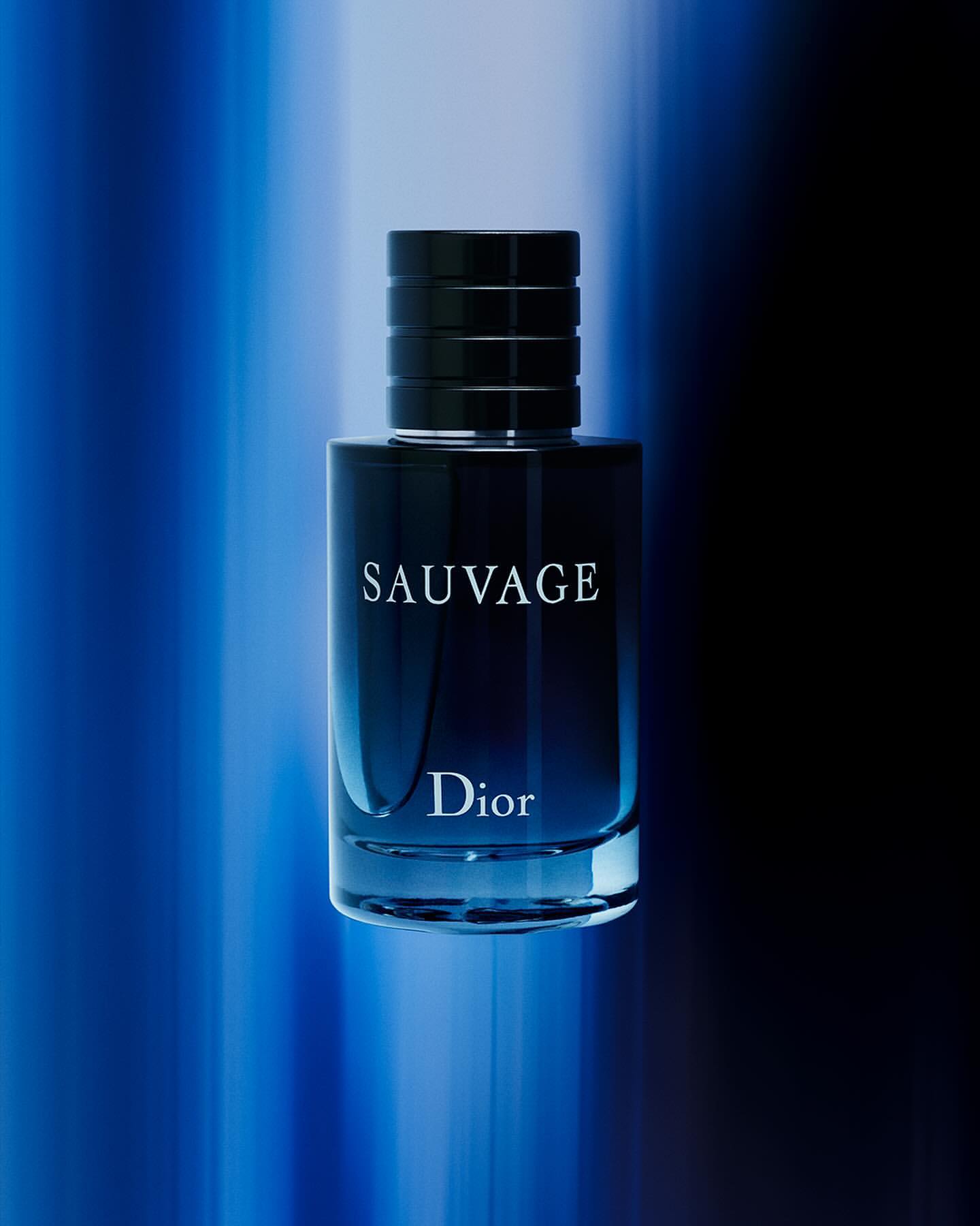 Close-up studio shot of a blue-tinted Sauvage Dior perfume bottle with a black cap against a blurred blue and black backdrop.