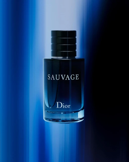 Close-up studio shot of a blue-tinted Sauvage Dior perfume bottle with a black cap against a blurred blue and black backdrop.