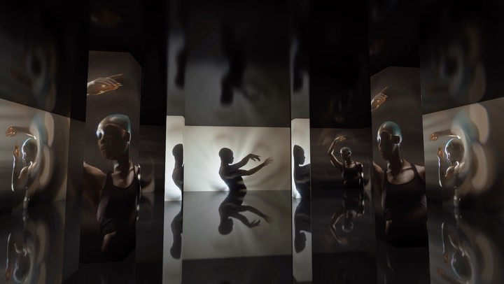 Person in a dark tank top stands against a bright white wall, reflected in dark mirror panels, creating an illusion of multiple figures.