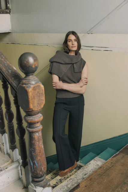 A woman stands on weathered stairs in a cozy, casual outfit, featuring a dark top, wide-leg pants, and eye-catching oversized scarf.