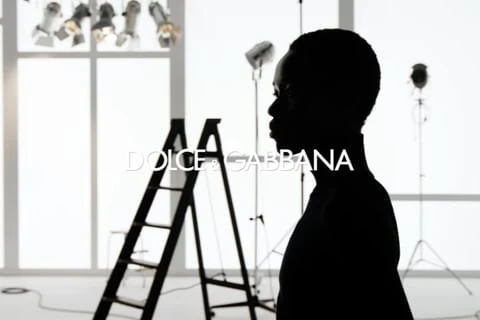 Black and white studio shot of a silhouetted figure and ladders, with lighting equipment and a Dolce & Gabbana logo.