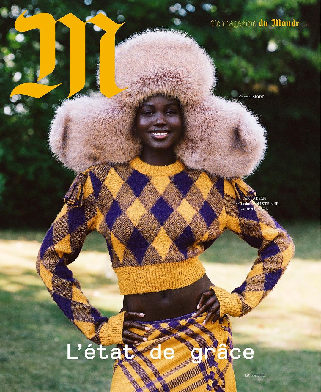 Model wearing a large furry hat and yellow and purple argyle sweater outdoors