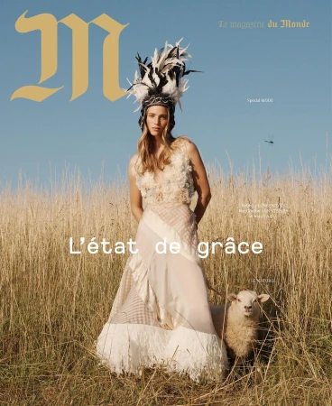 Magazine cover featuring a woman in couture gown with feather headdress standing in a field next to a sheep on a sunny day.