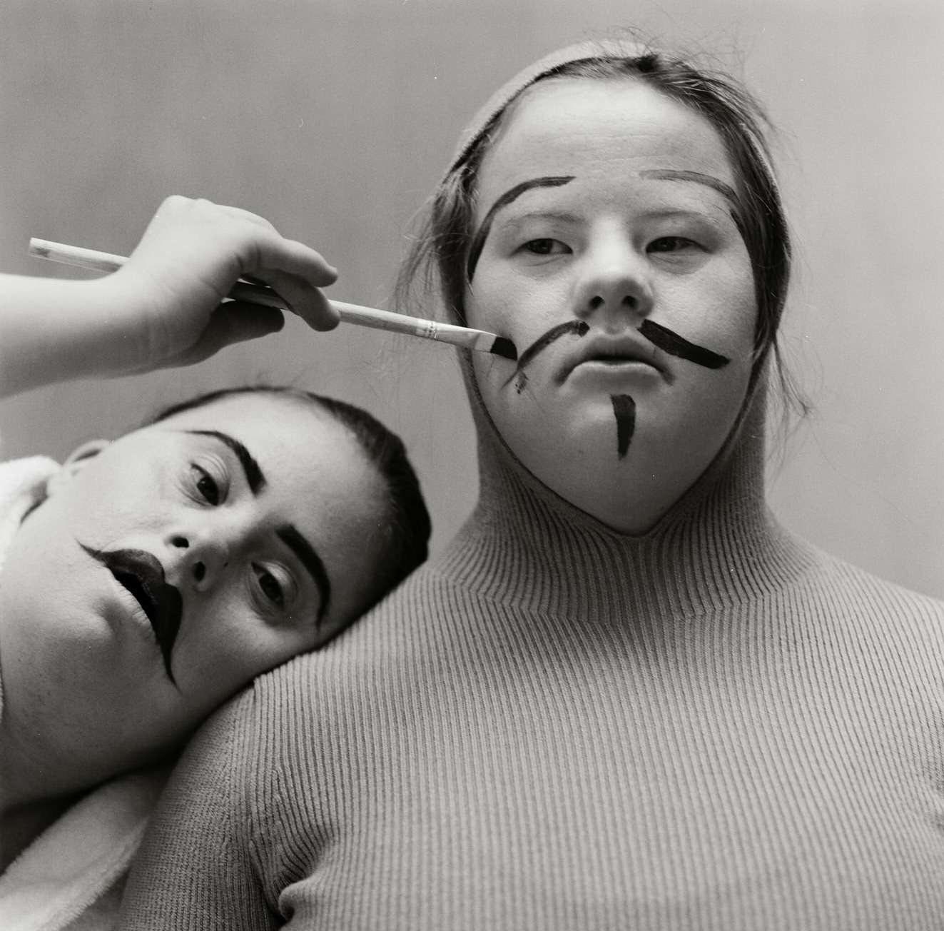 Two people getting their makeup done with a brush in a studio setting. Dark theatrical makeup is being applied to their faces.