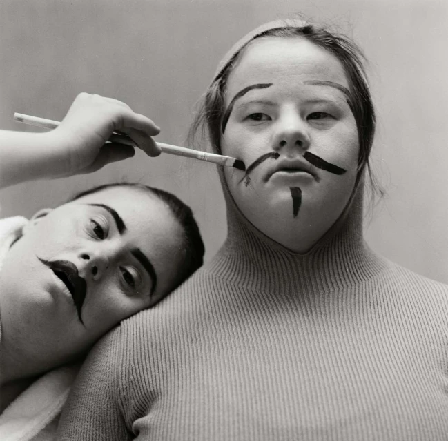 Two people getting their makeup done with a brush in a studio setting. Dark theatrical makeup is being applied to their faces.