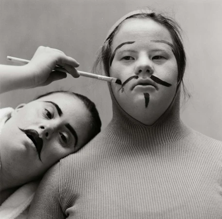 Two people getting their makeup done with a brush in a studio setting. Dark theatrical makeup is being applied to their faces.
