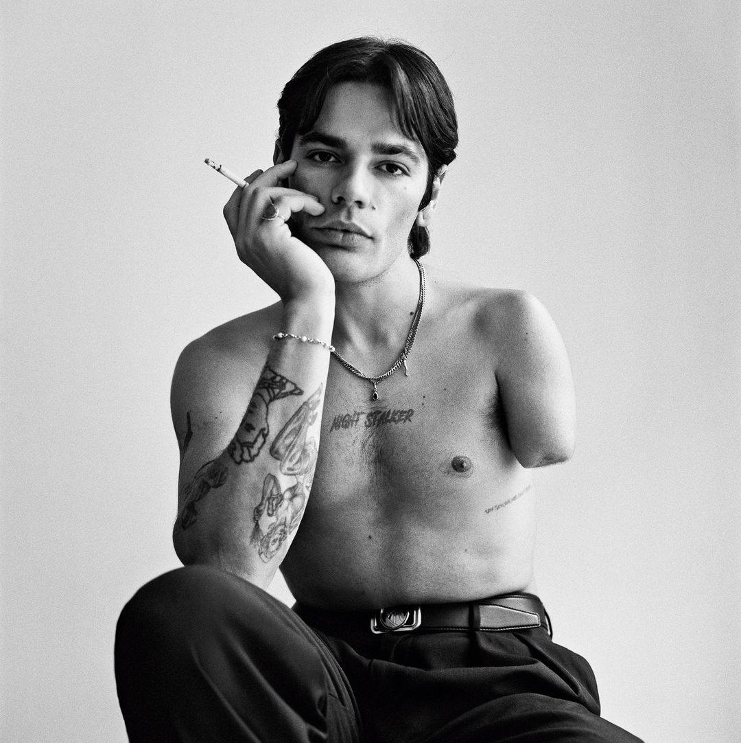 Portrait of a tattooed shirtless man with dark hair holding a cigarette to his face, photographed by Gorka Postigo in Paris.