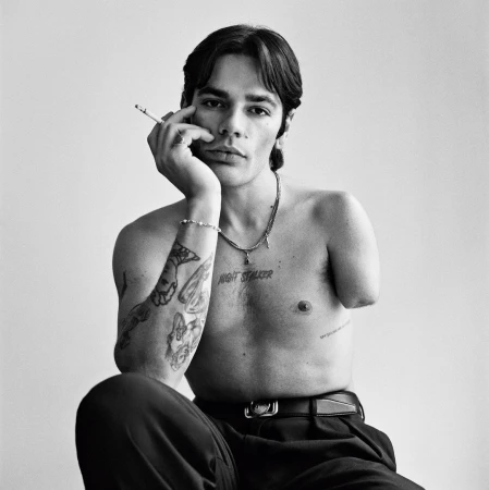 Portrait of a tattooed shirtless man with dark hair holding a cigarette to his face, photographed by Gorka Postigo in Paris.