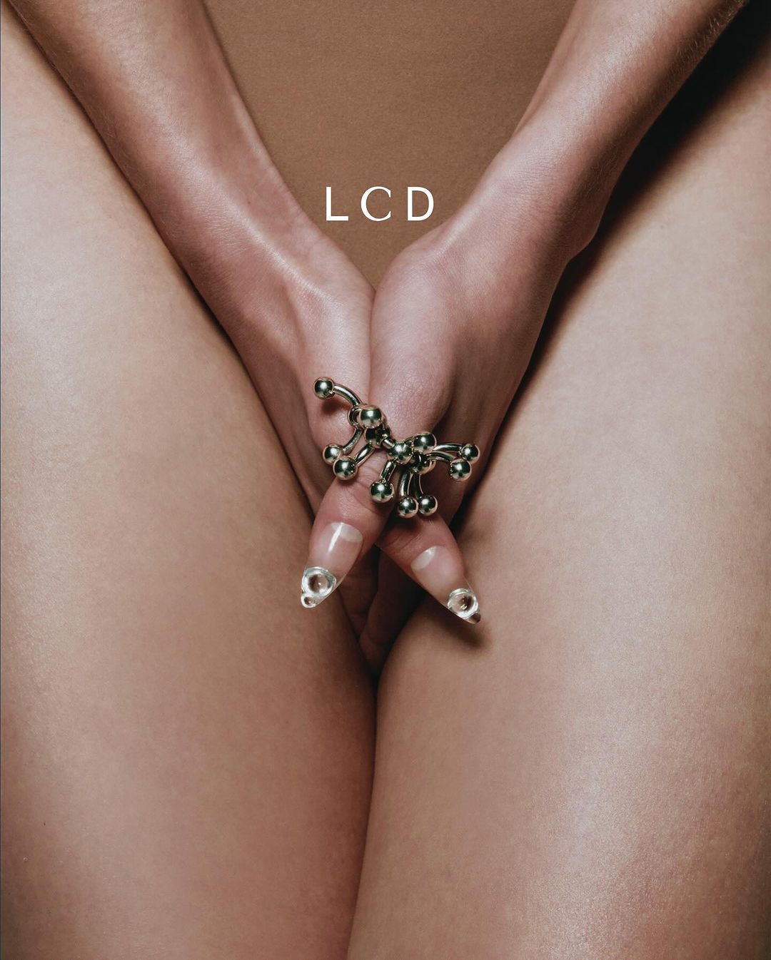 Close-up studio shot of a woman's hands with a ring, nude skin, and neutral beige background, highlighting beauty and fashion.