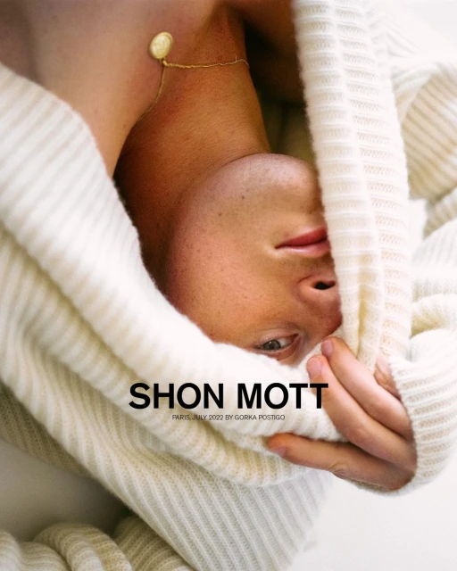 Close-up studio shot of a fair-skinned adult male wearing a knit hoodie, with fair lighting and a gold necklace.