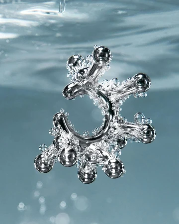 A silver metal jack toy is suspended in the center of light blue water filled with tiny clear bubbles in an eye-level shot.