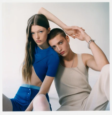 Two young fashion models pose in a photo studio wearing matching knitted outfits in cobalt blue and light beige against a white backdrop.