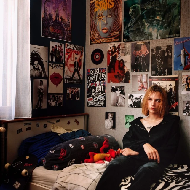 Teenager sits on a zebra-print bed in a bedroom decorated with posters. The room shows a young person's interest in music and pop culture.