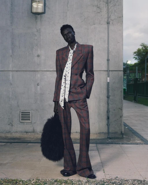 Fashionable adult male model wearing plaid suit, patterned tie, and holding a fur purse outdoors in an editorial fashion shoot.