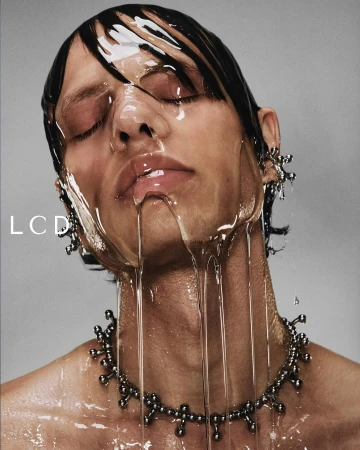Close-up portrait of a man with wet hair and honey dripping over his face wearing a silver necklace against grey backdrop