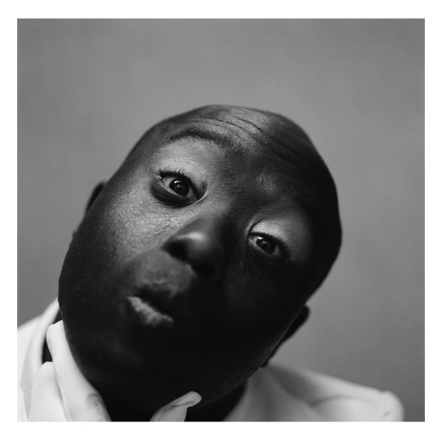 Close-up black and white portrait of an African American adult male looking up with a slight smirk and white shirt collar visible.