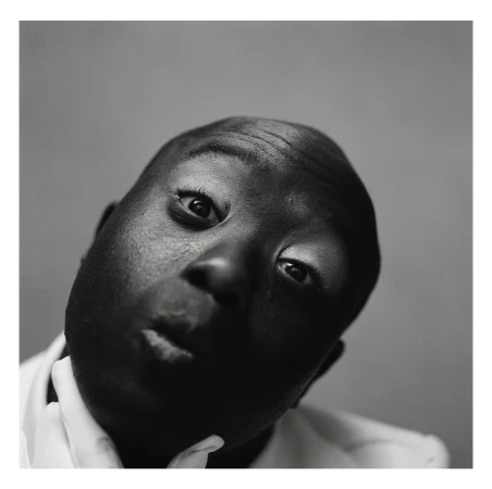 Close-up black and white portrait of an African American adult male looking up with a slight smirk and white shirt collar visible.