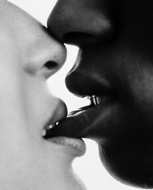 Close-up studio shot of two faces in contrasting tones, with lips touching, emphasizing diversity and intimate connection in black and white.