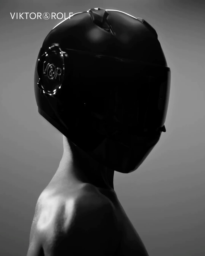 Fashion shot featuring a person wearing a black helmet and posing against a grey background. Viktor & Rolf logo visible in the upper left.