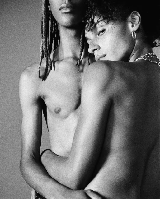 Black and white studio portrait of two androgynous people embracing, showcasing raw emotion and intimate connection against a neutral backdrop.