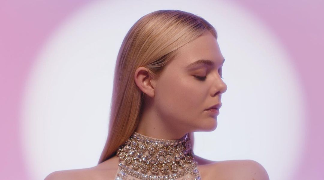 Elegant woman with fair skin, blonde hair in a side profile wearing a diamond studded collar against a soft pink studio backdrop.