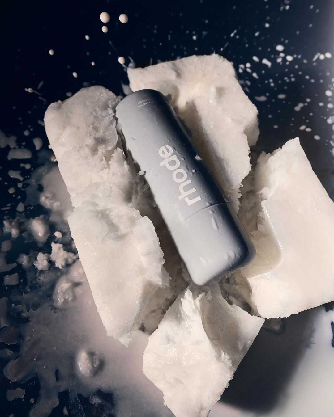 Close-up of Rhode brand lip balm on ice, showcasing beauty and skincare in cool tones, emphasizing product presentation and minimalism.