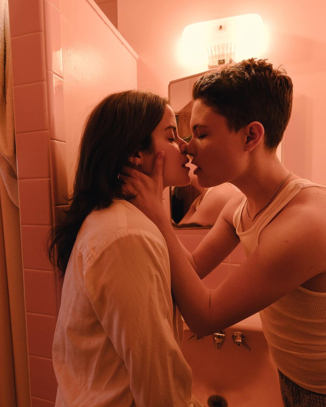 Two young adults share an intimate kiss in a brightly lit bathroom, showcasing a close and tender moment between the couple.