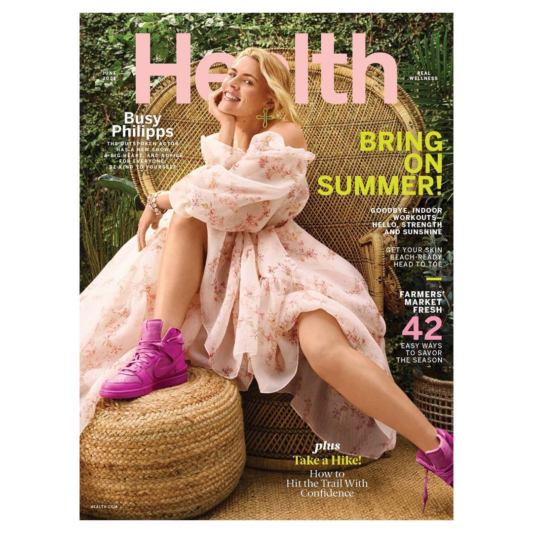 Health magazine cover featuring Busy Philipps in a floral dress, sitting on a wicker chair, with pink sneakers and lush green background.