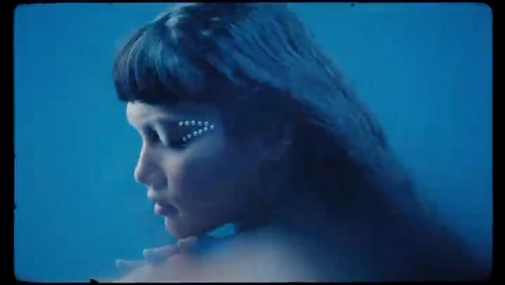 Close-up of a woman with embellished makeup, against a teal backdrop, captured with soft lighting and a shallow depth of field.