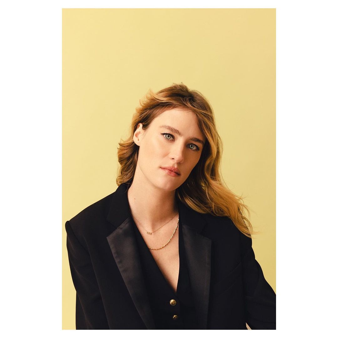 Portrait of adult female with light hair in black blazer against yellow studio backdrop. Fashion and beauty shot, eye-level angle, indoors.