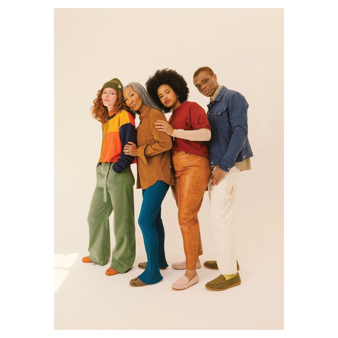 Four diverse people in casual clothing stand in a row against a cream backdrop. A warm-toned studio shot emphasizes textures and earthy colors.
