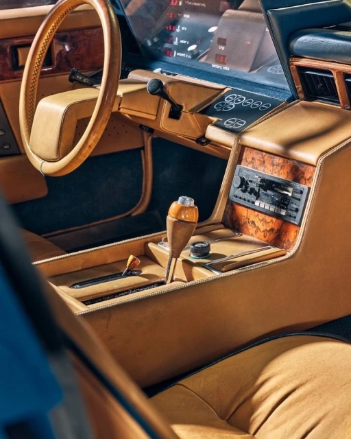 Interior of a classic car featuring a tan leather dashboard, steering wheel, and center console with wooden accents and retro radio.