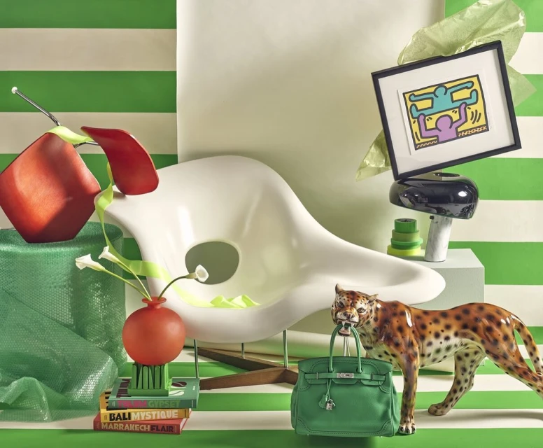 Still life composition with green stripes featuring a white chair, framed artwork, flower vase, and a leopard statue carrying a purse.