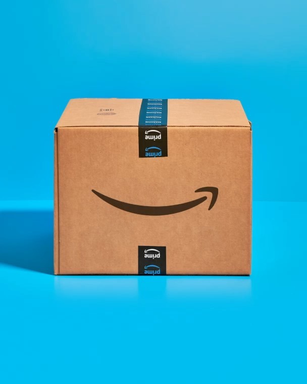 Amazon Prime cardboard box on a blue surface, featuring the Prime logo and tape, in a studio setting with controlled lighting.