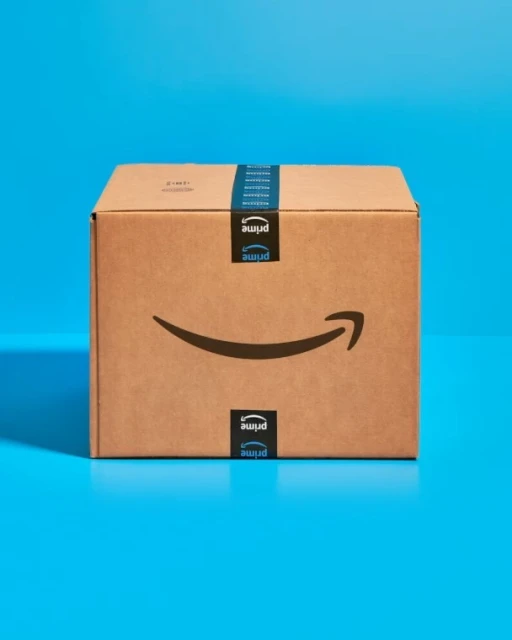 Amazon Prime cardboard box on a blue surface, featuring the Prime logo and tape, in a studio setting with controlled lighting.