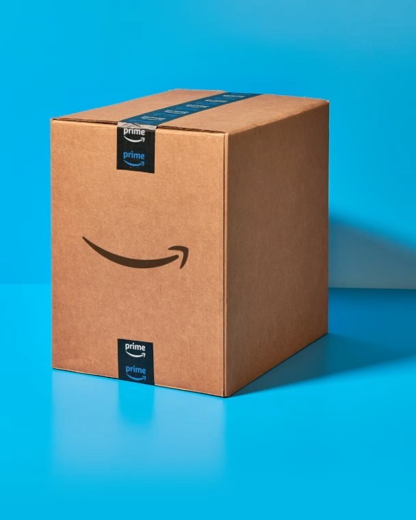 Amazon Prime box on blue surface, sealed with branded tape, studio-lit shot with clean background, product shot for e-commerce or delivery.