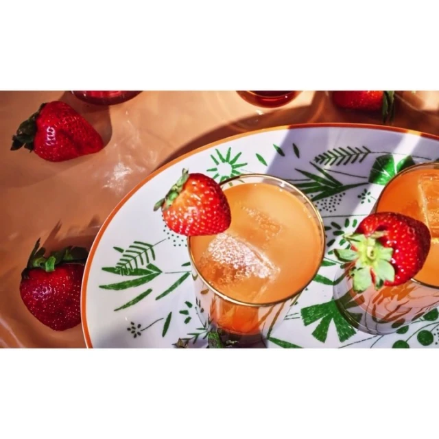 Two orange cocktails garnished with strawberries on a leaf-patterned tray in soft, diffused lighting, creating a refreshing and vibrant scene.