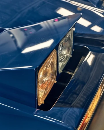 Close-up of a blue vintage car's headlight assembly featuring the car's painted body and dual headlights.