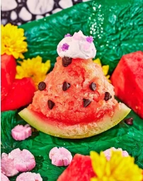 Close-up food photography of a slice of watermelon styled like a dessert with chocolate chips, whipped cream, and sprinkles.