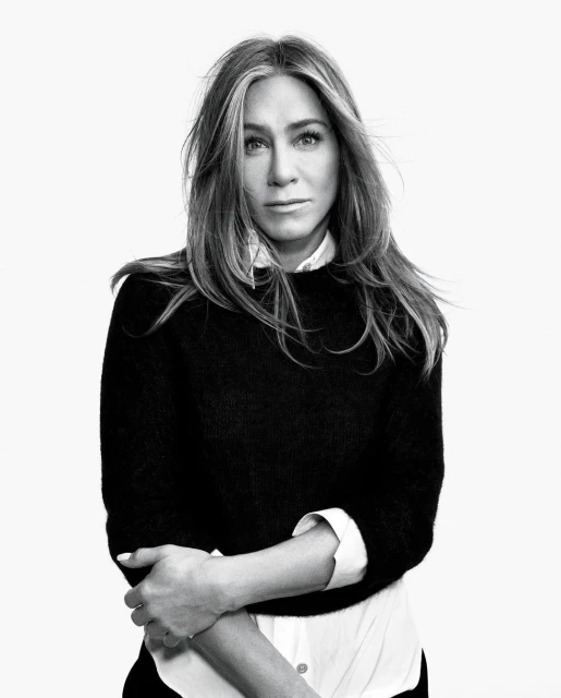 Black and white portrait of Jennifer Aniston with long brown hair and wearing a layered white collared shirt and black sweater.