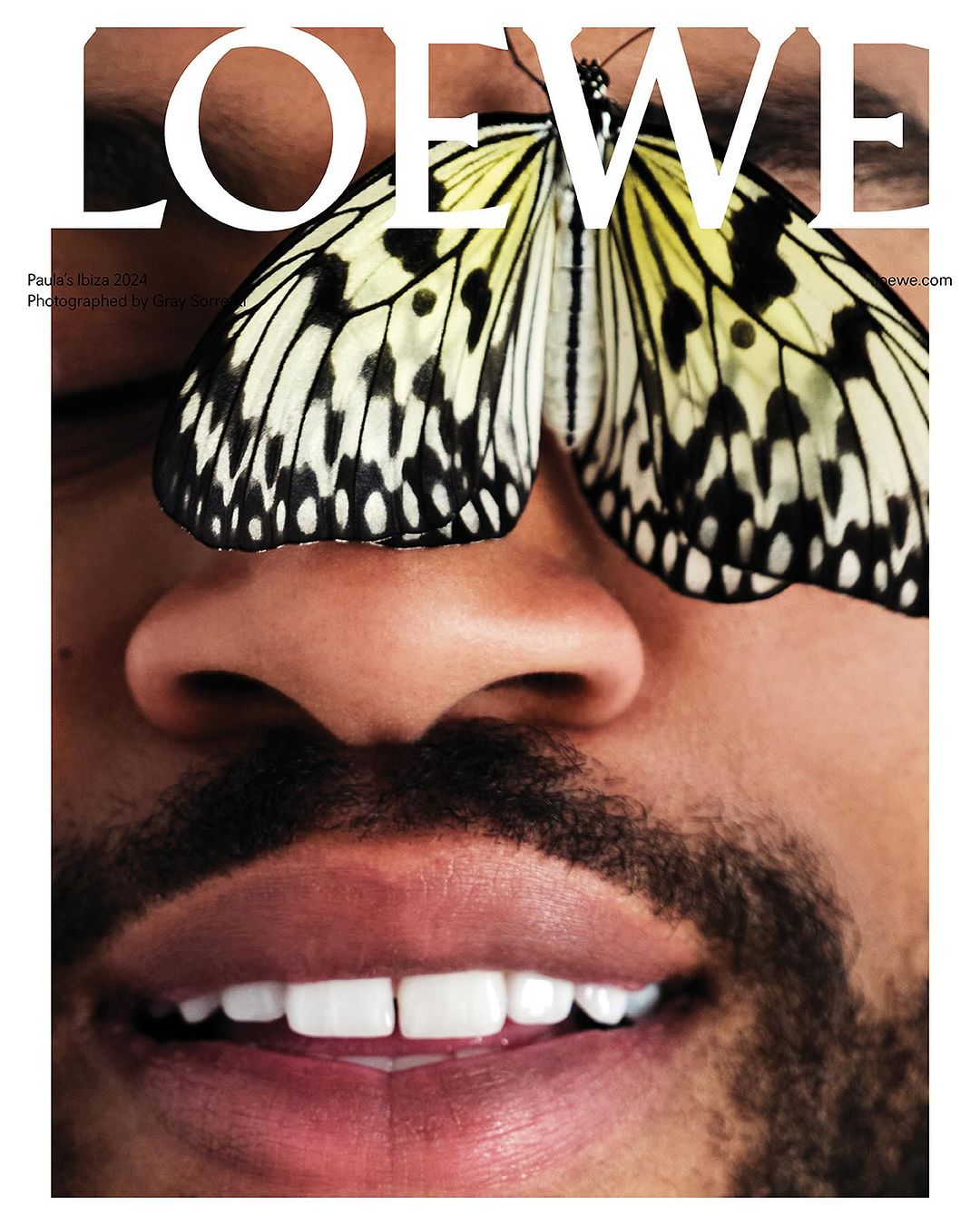 Close-up of a face with a butterfly perched on the nose, partially covering the eyes, under the brand logo LOEWE, fashion photography.